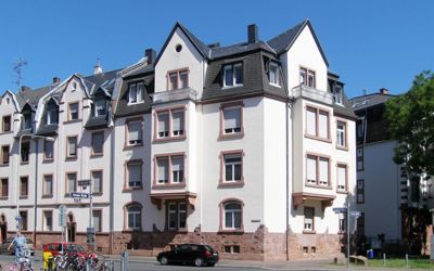 Von Immobilienbewertung Westenberger begutachtetes Altbau-Mehrfamilienhaus in einer urbanen Wohngegend. Der Sockel und die Fenstergewänder sind aus rotem Sandstein. Außenwände sind in beige Farbe gestrichen. Das Mansarddach mit schwarzem Schiefer bedeckt.